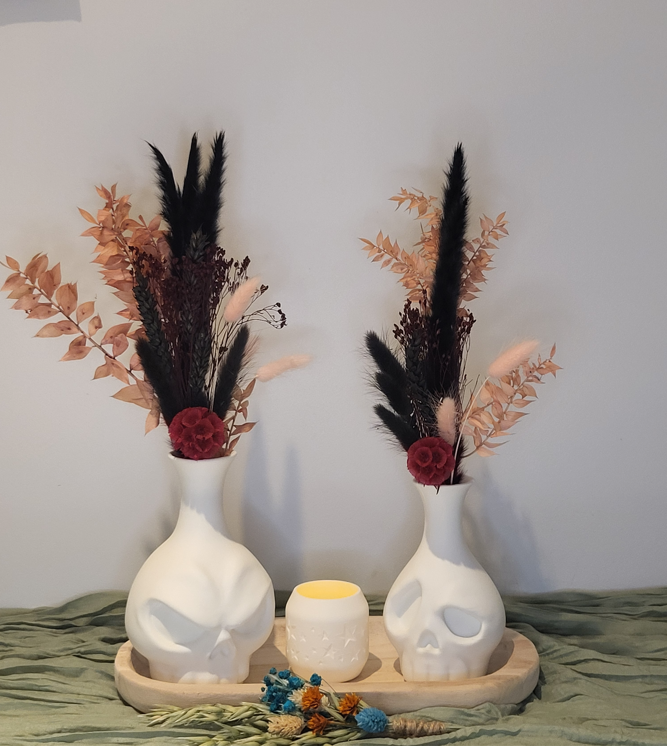 Skull vaasjes gevuld met droogbloemen en theelichthouder op houten schaal.