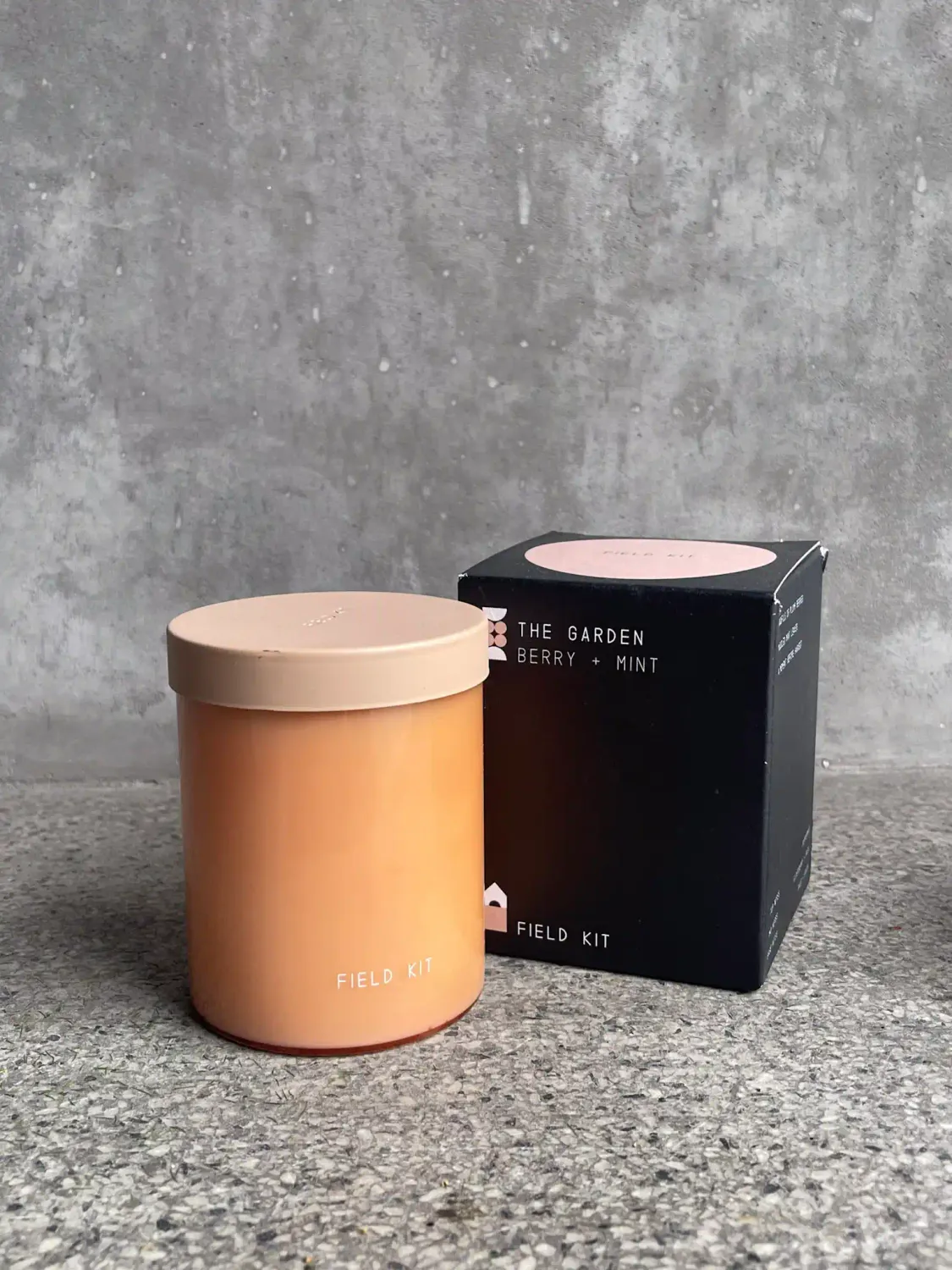 The Garden Berry + Mint soy candle in amber glass jar with pink lid next to black gift box