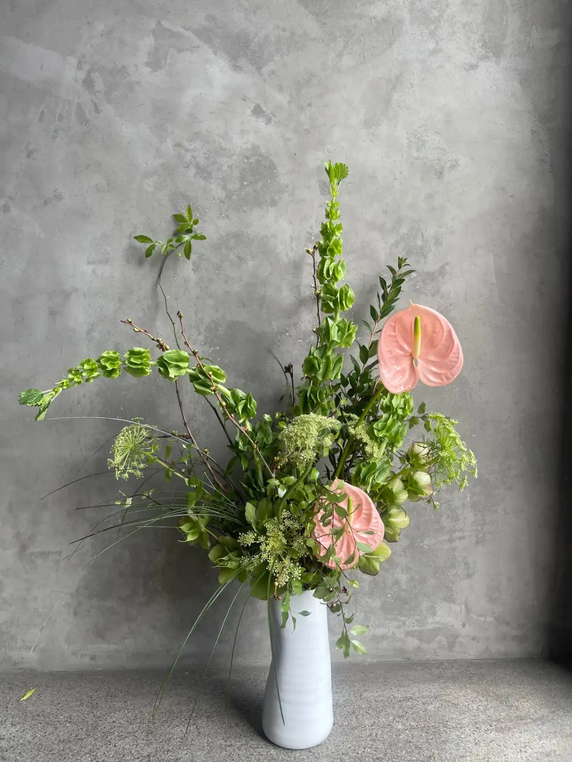 Vogue arrangement featuring pink anthuriums, bells of Ireland, Queen Anne's lace, and lush greenery in a sculptural editorial