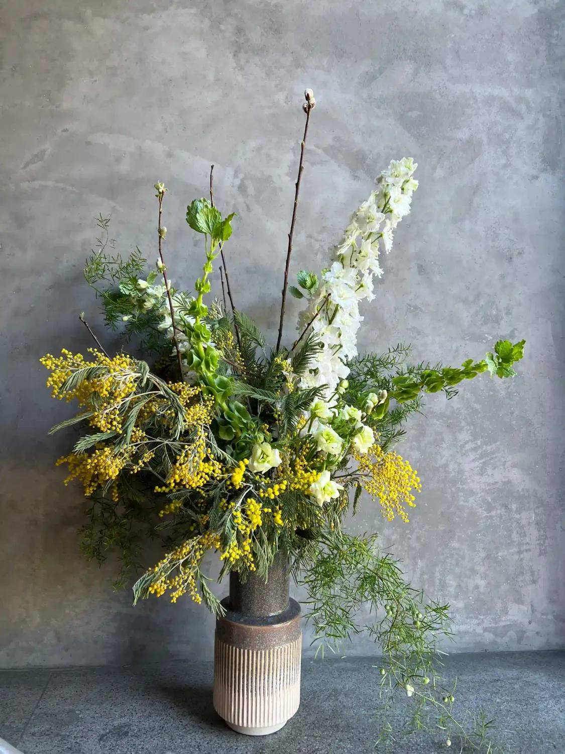 Foyer arrangement with white delphinium, yellow acacia, pussy willow branches, and green viburnum in a sculptural garden st