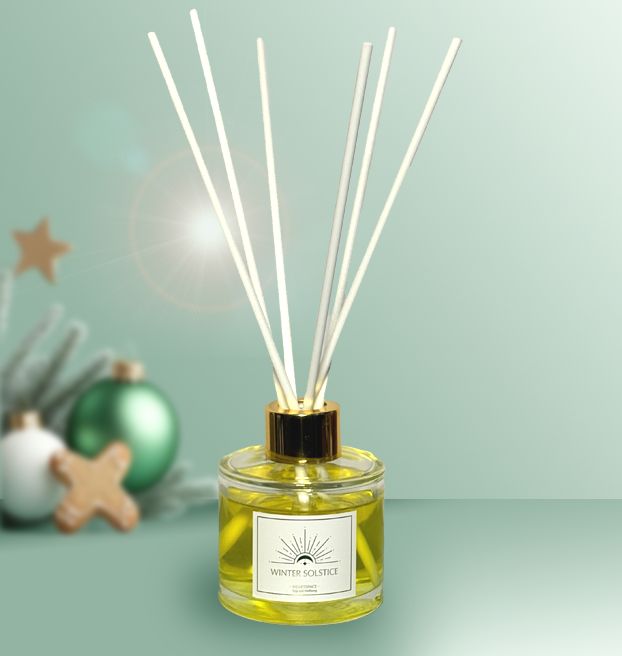 Product shot of HeartSpace 'Winter Solstice' reed diffuser in glass bottle with gold neck on festive background.