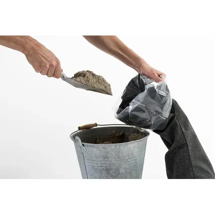 Handen die met een schep zand in een zwarte zandzak scheppen
