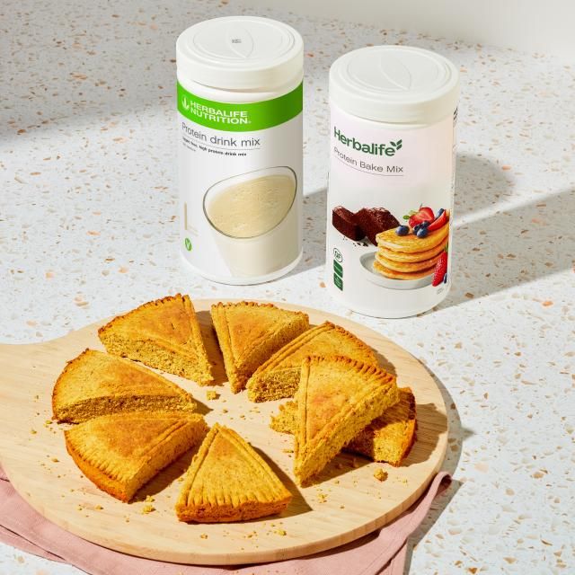 ProteinKit con barattolo di Protein Bake e Protein Drink Mix Vegan di Herbalife Nutrition su un tavolo con una torta tagliata.