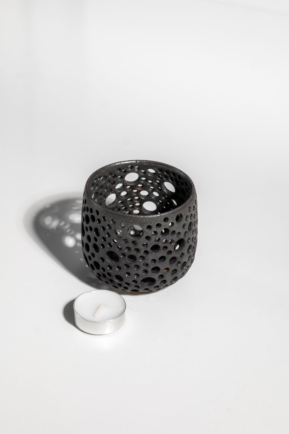 Brutalist contemporary matte black stoneware ceramic candleholder that projects shadows resembling starry night sky.