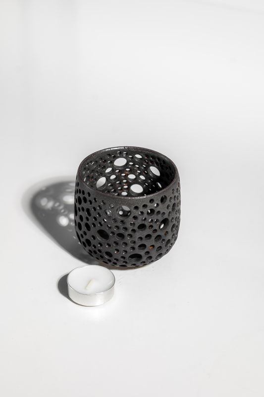 Brutalist contemporary matte black stoneware ceramic candleholder that projects shadows resembling starry night sky.