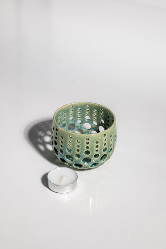 Beachy ocean blue green ceramic candleholder that has pierced holes to allow light to shine through the walls and cast shadow