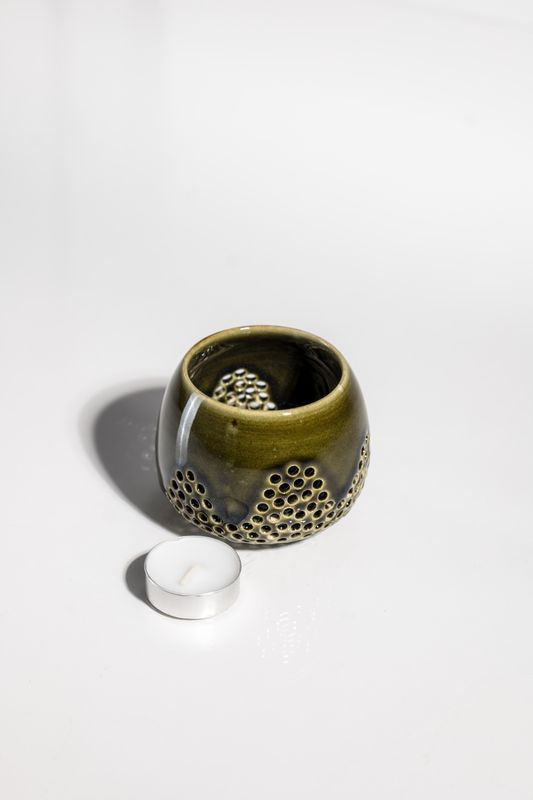 Dark sage green ceramic candle holder with pierced holes flowing around the edges allowing light to shine through the walls.
