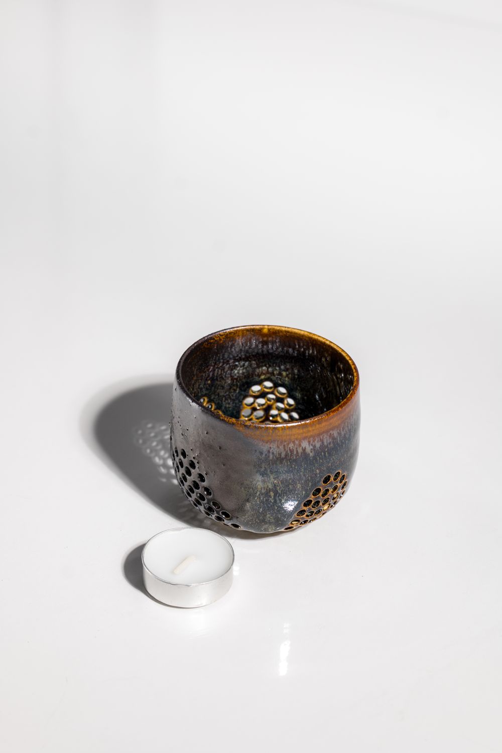 Organic ceramic candleholder hand thown and pierced in a ceramic studio. Volcanic glazing gives this variation and depth