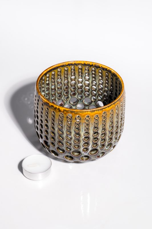 Large pierced ceramic candleholder with variated size holes that allow for light to shine through the walls when lit.