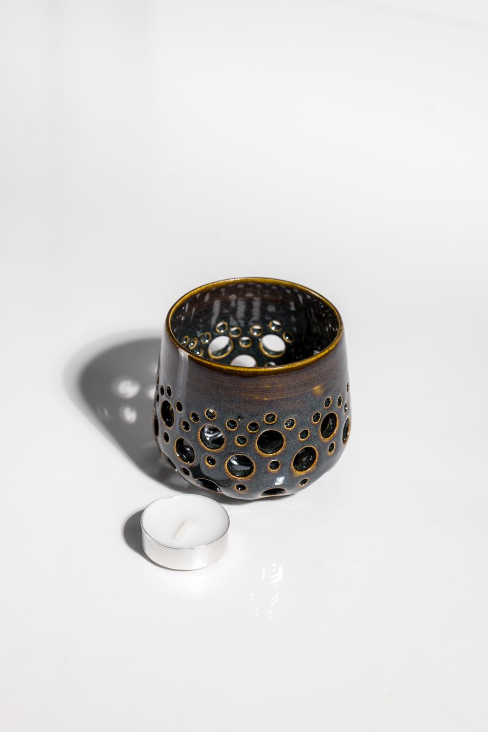 Ceramic candleholder with holes punched in it to allow light to shine from the tealight candle. handmade in the USA by locals