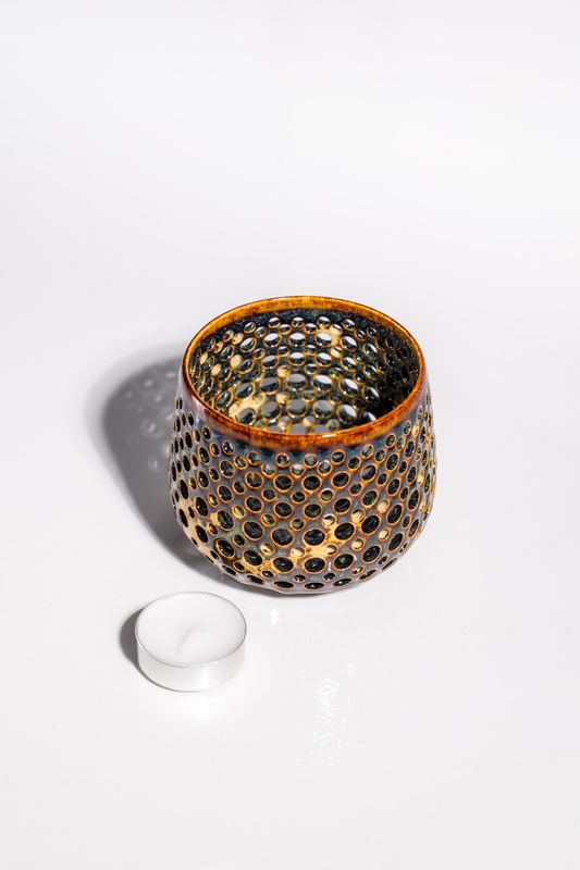 Ceramic glossy candleholder with organic variations. Hand pierced holes that allow light to shine through and cast shadows.