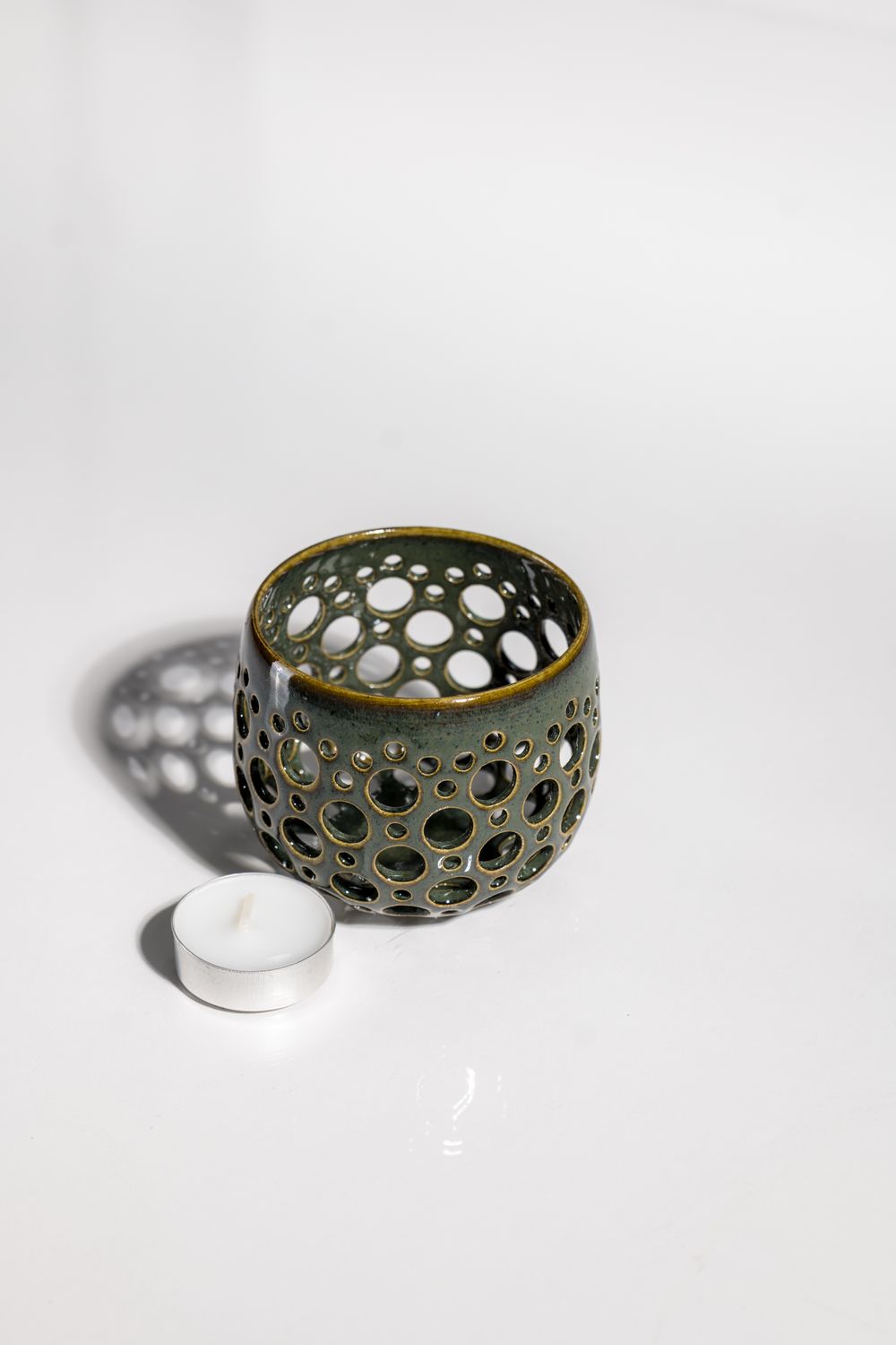 Light and airy dark green ceramic hurricane votive holder. With hand punched holes light shines through casting shadows.