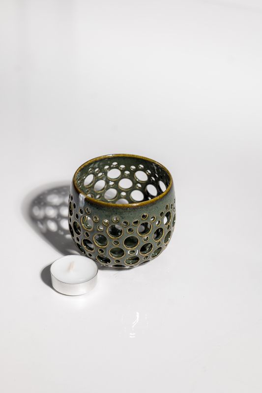 Light and airy dark green ceramic hurricane votive holder. With hand punched holes light shines through casting shadows.