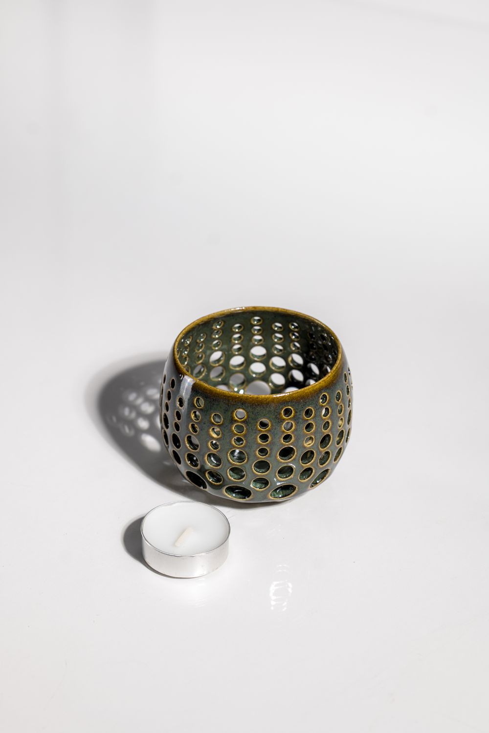 Artisinally made candleholder that casts light across the room in starlight patteryn with brown green glaze. 