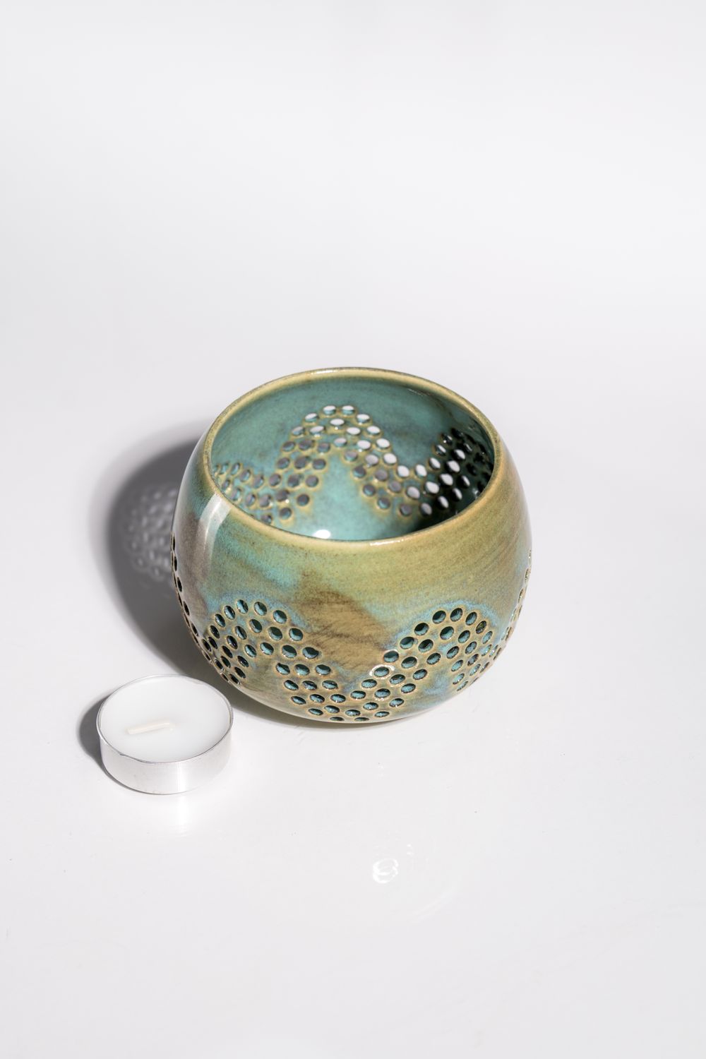 Rustic ceramic candleholder for tealight or votive candles. Designed to cast shadows and light on the wall around it.