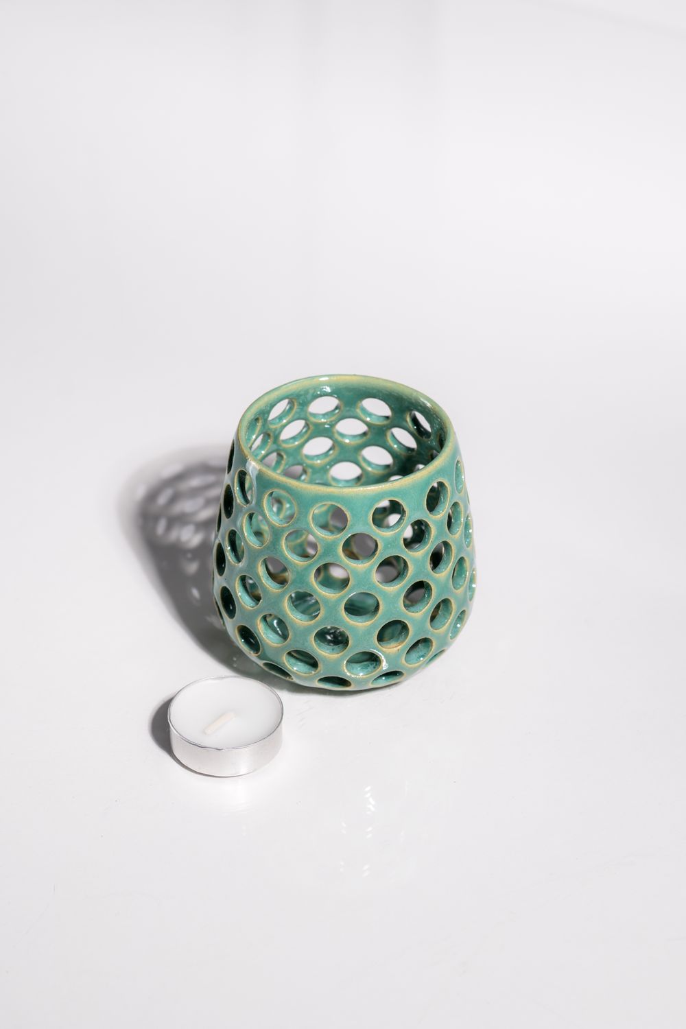 Cute sea foam ceramic candleholder with circles cut out to allow light to shine through from candle in the center. 