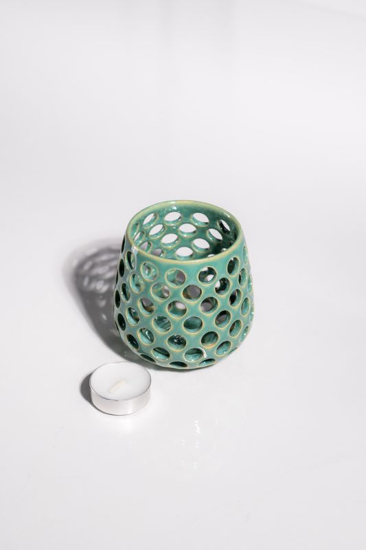 Cute sea foam ceramic candleholder with circles cut out to allow light to shine through from candle in the center. 