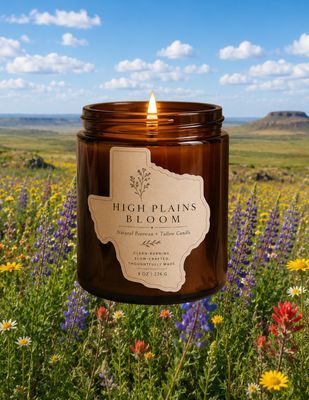 Lit amber glass candle labeled “High Plains Bloom” centered in a blooming wildflower field under a bright blue sky