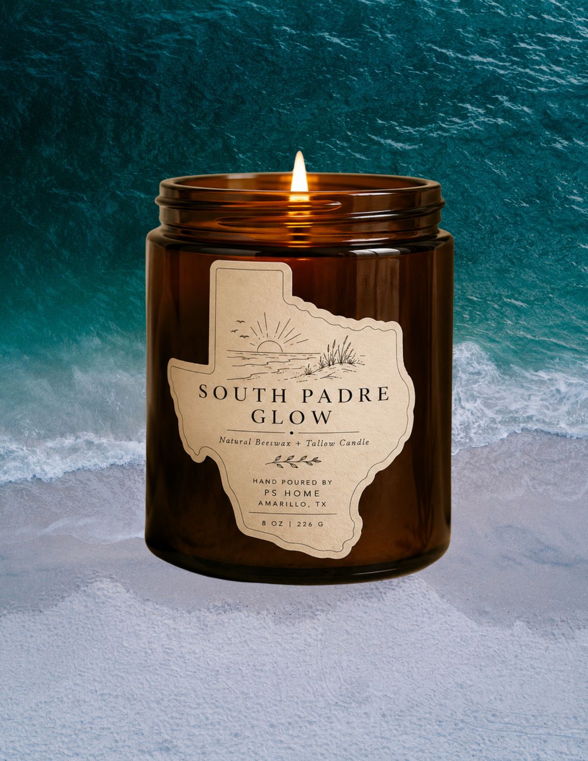 Lit amber glass candle labeled “South Padre Glow” set against an aerial ocean shoreline, with turquoise waves and white sand