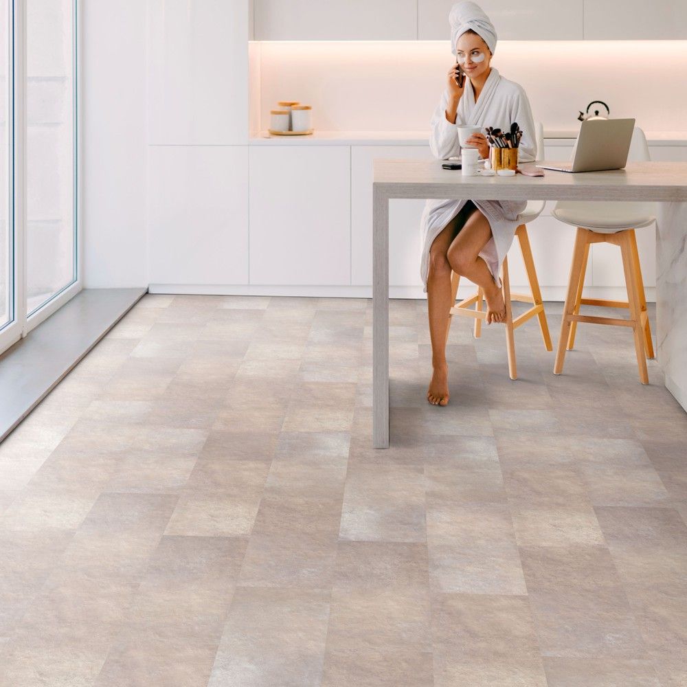 Klick-Vinyl in beiger Fliesenoptik in einer Küche. Am Tisch sitzt eine Frau. Myrcella