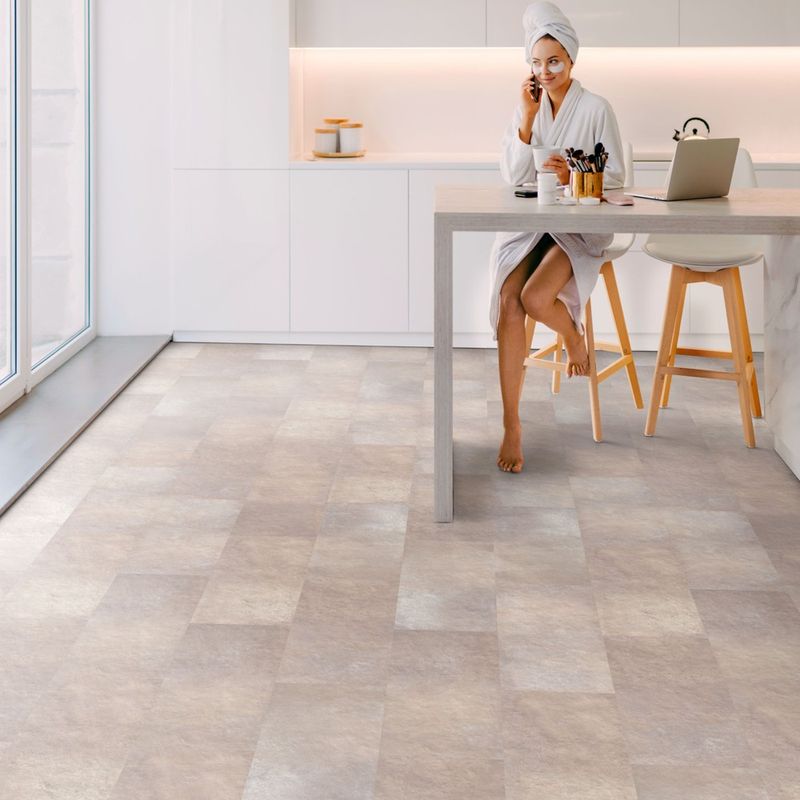 Klick-Vinyl in beiger Fliesenoptik in einer Küche. Am Tisch sitzt eine Frau. Myrcella