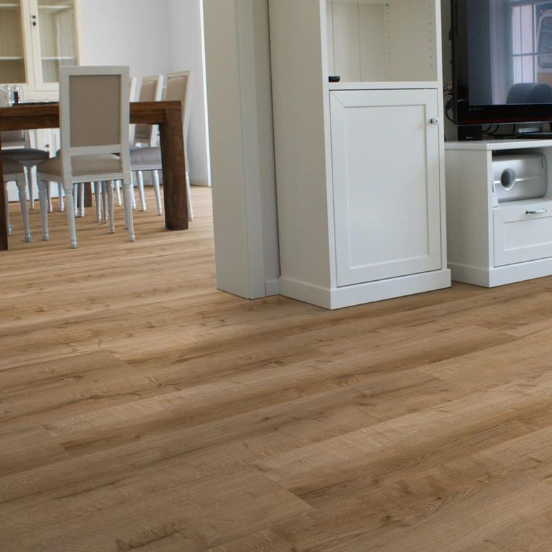Klick-Vinyl in brauner und natürlicher Eichenholzoptik in einem Wohnzimmer mit sichtbarem Essbereich im Hintergrund. 