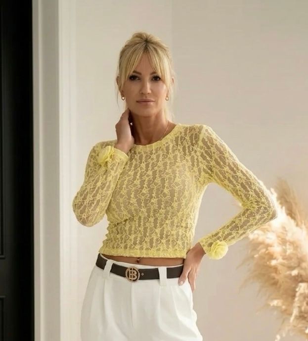 Kobieta w jasnożółtej koronkowej bluzce Bibione z długim rękawem, ozdobionej różami przy mankietach.