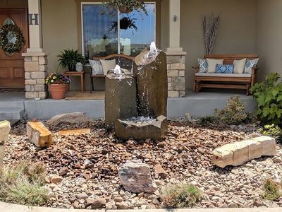 Twin basalt column bubbler fountain spilling into a river rock bed at a home's front entry.
