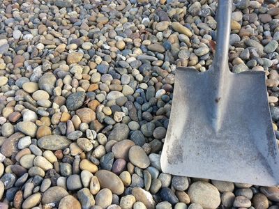 Round river pebbles in mixed tan, grey and rust tones with a shovel blade set in for scale.