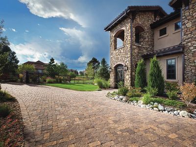 Cobblestone paver driveway curving past boulder-lined beds to a stone and stucco home.