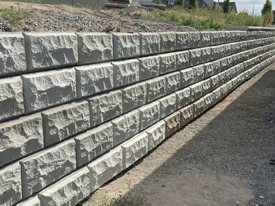 Five-course World Block retaining wall running along a gravel side yard under a blue sky.