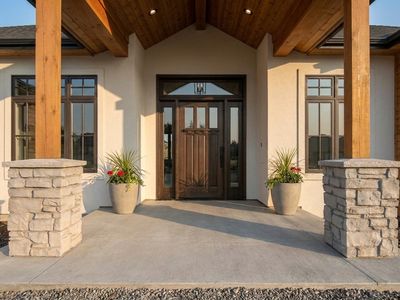 Stacked stone porch columns with cast caps flanking a craftsman entry, with matching planters and a broom-finish concrete sla