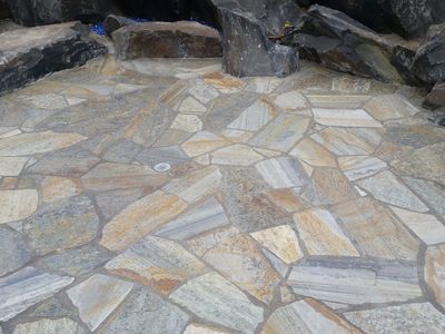 Finished flagstone patio in gold and silver tones with mortared joints and a dark basalt border.