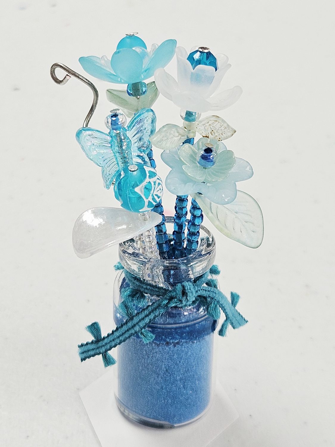 Blue beaded flowers in glass vase with blue sand