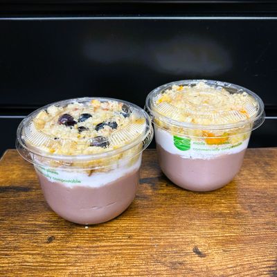 Two cups of the Locavore Store&#39;s poi-faits. Half filled with fresh poi and a thick layer of in-house made coconut cream, topped with bananas and macadamia nuts. One cup has blueberries on top and the other has poha berries.