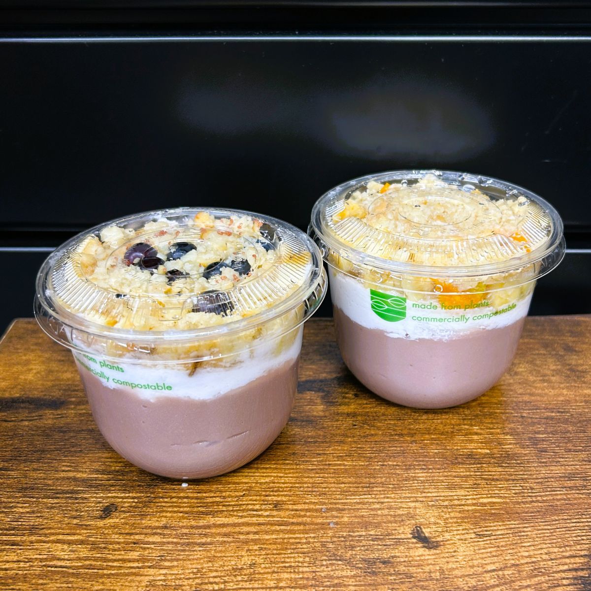Two cups of the Locavore Store's poi-faits. Half filled with fresh poi and a thick layer of in-house made coconut cream, topped with bananas and macadamia nuts. One cup has blueberries on top and the other has poha berries.