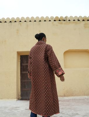 Model wearing long, quilted, fully reversible and handblock printed jacket designed by Christine Bekaert, brown base
