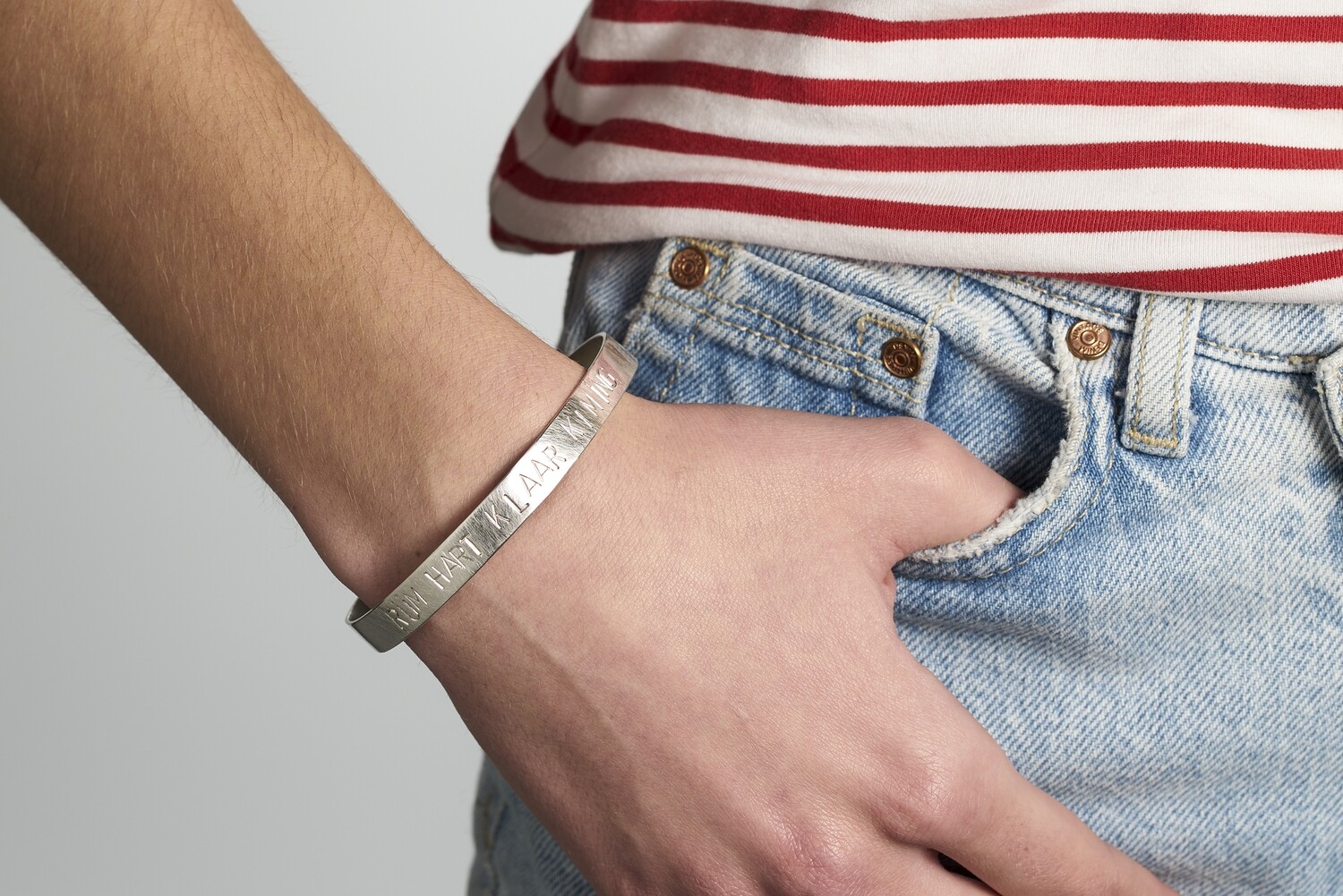 Handgelenk einer jungen Frau. Sie trägt einen Armreif aus Silber mit dem Schriftzug RÜM HART KLAAR KIMING.