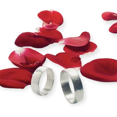 Zwei Silberringe mit gehämmerter Oberfläche, sie stehen auf Rosenblättern.