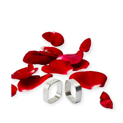 Eckige Trauringe aus mattiertem Silber. Stehend auf Rosenblättern.