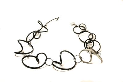 Collier aus großen, schwarzen Kettengliedern, die an Wellen erinnern. Ein Kettenglied ist hell.