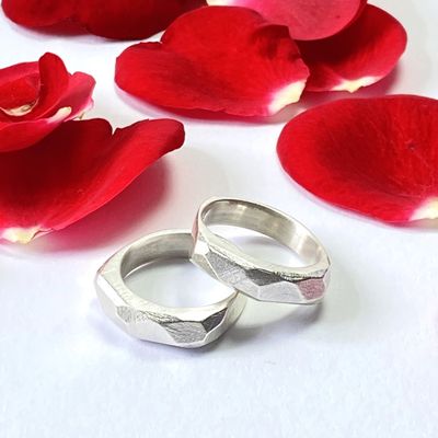 Zwei Silberringe auf Rosenblättern. Die Oberfläche ist grob facettiert.