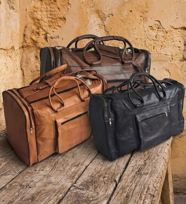 Drei handgefertigte Ziegenleder-Reisetaschen der Horizontal Classic Serie in den Farben Cognac, Dunkelbraun und Schwarz auf e