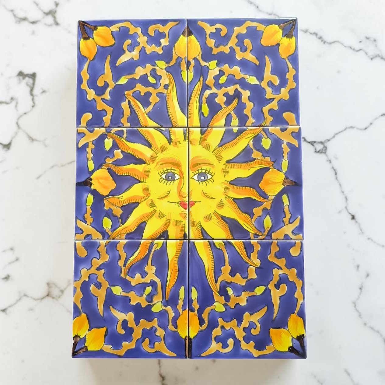 Mediterranes Fliesenbild mit gelber Sonne komplett an einer weißen Wand montiert als dekorativer Blickfang im Raum.