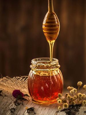 Golden honey dripping from a wooden honey dipper into a glass jar, representing Urban Market 1919's honey collection.