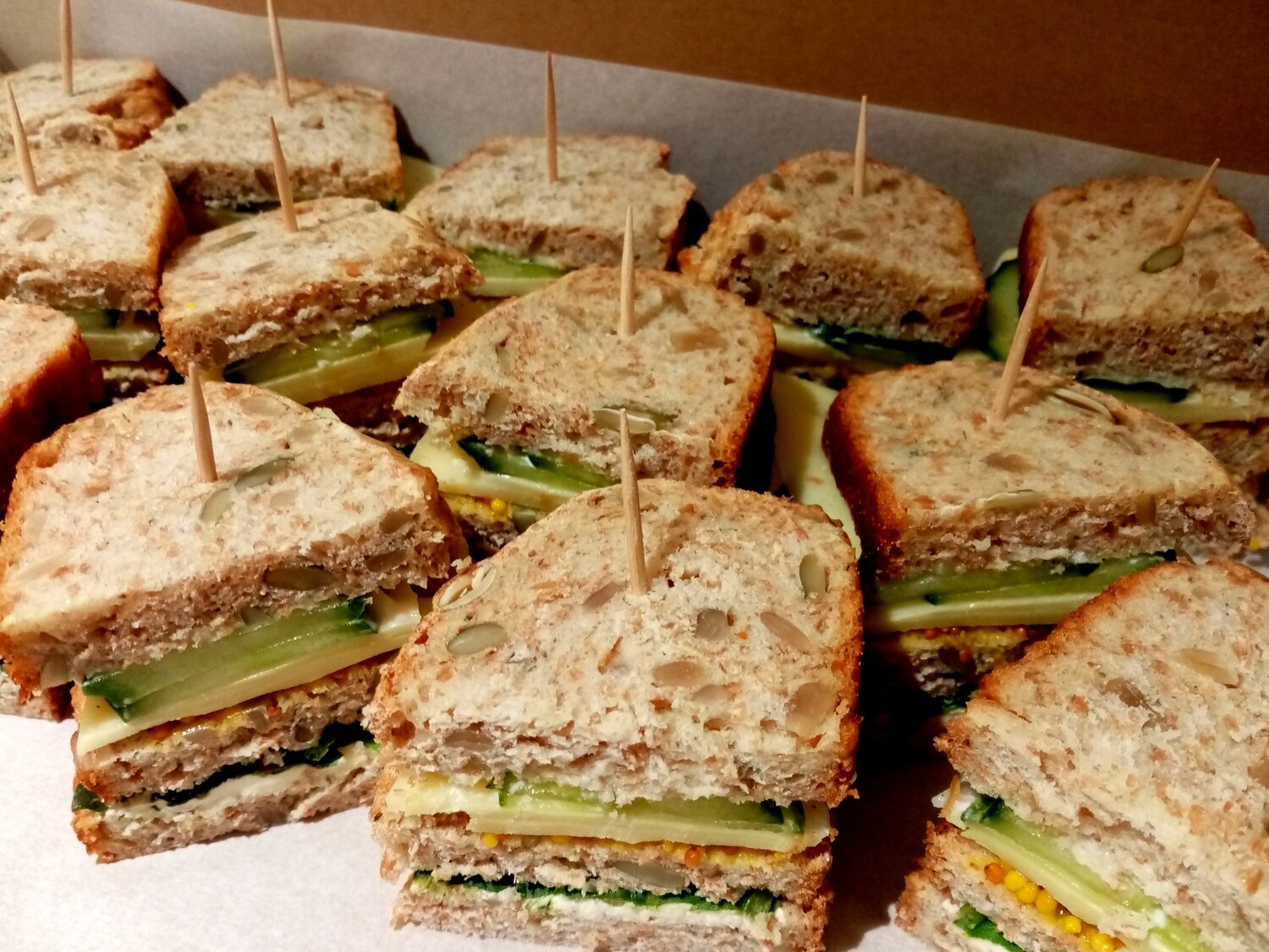 10x mini wholemeal spelt and seed club sandwiches with cream cheese, edam, mustard, cucumber, mayonnaise and greens.