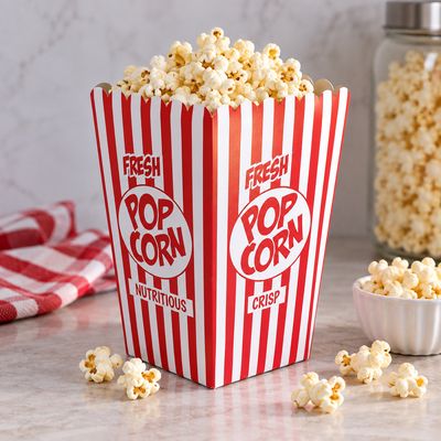 Classic red and white striped popcorn box overflowing with fresh popcorn on a marble counter next to a glass jar.