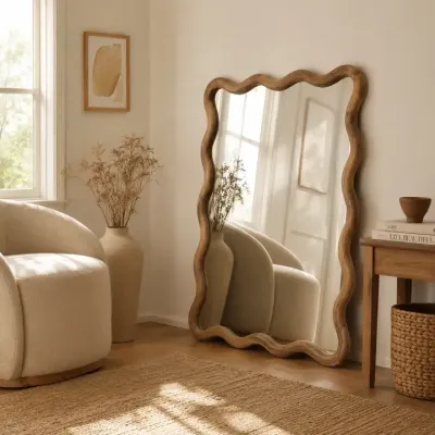 Wavy wood-framed wall mirror beside a cream armchair in a sunlit room