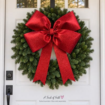 Giant red glitter Christmas bow styled on an evergreen wreath on a white front door.