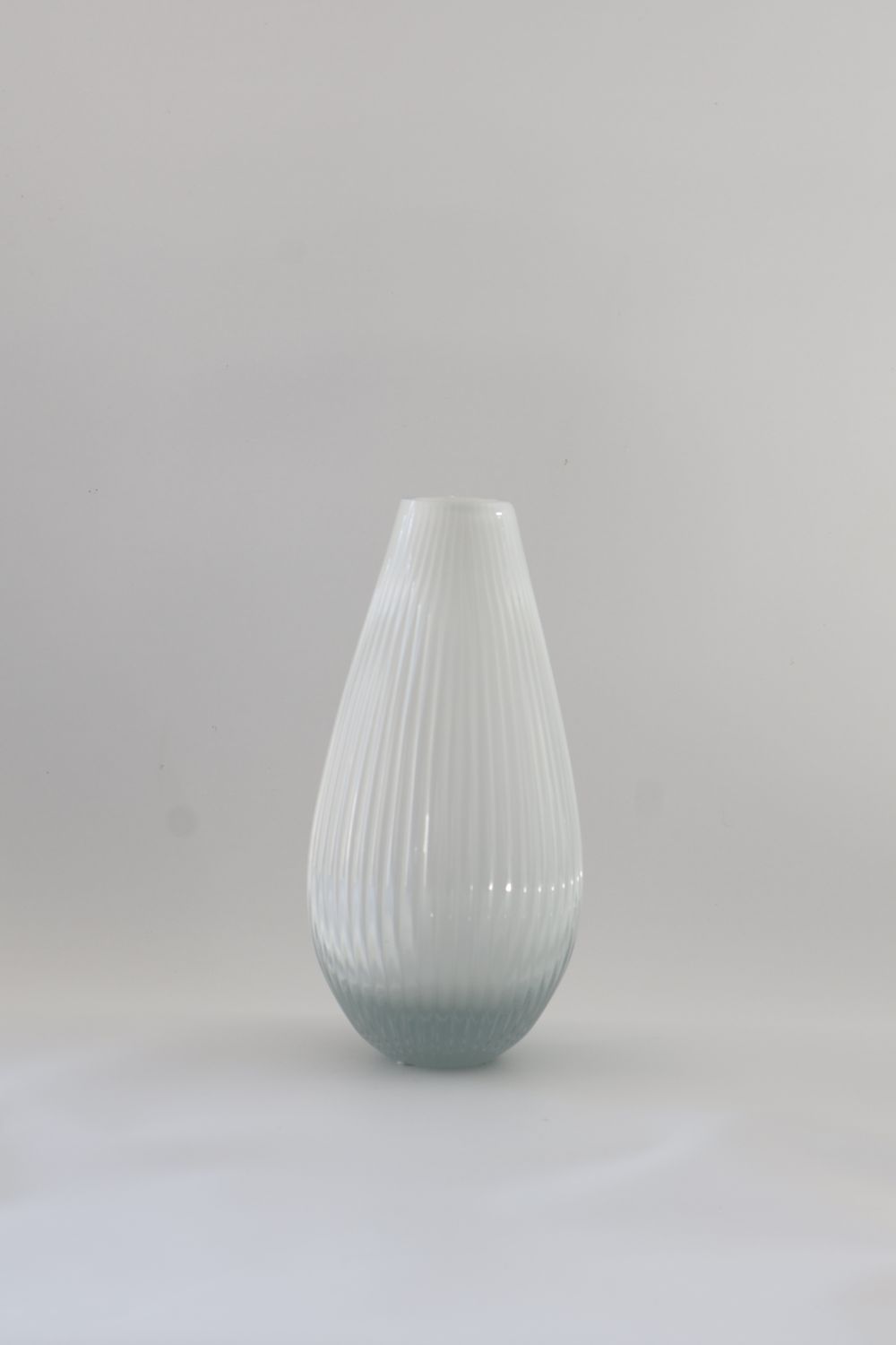 White glass vase features a teardrop design with vertical fluting.